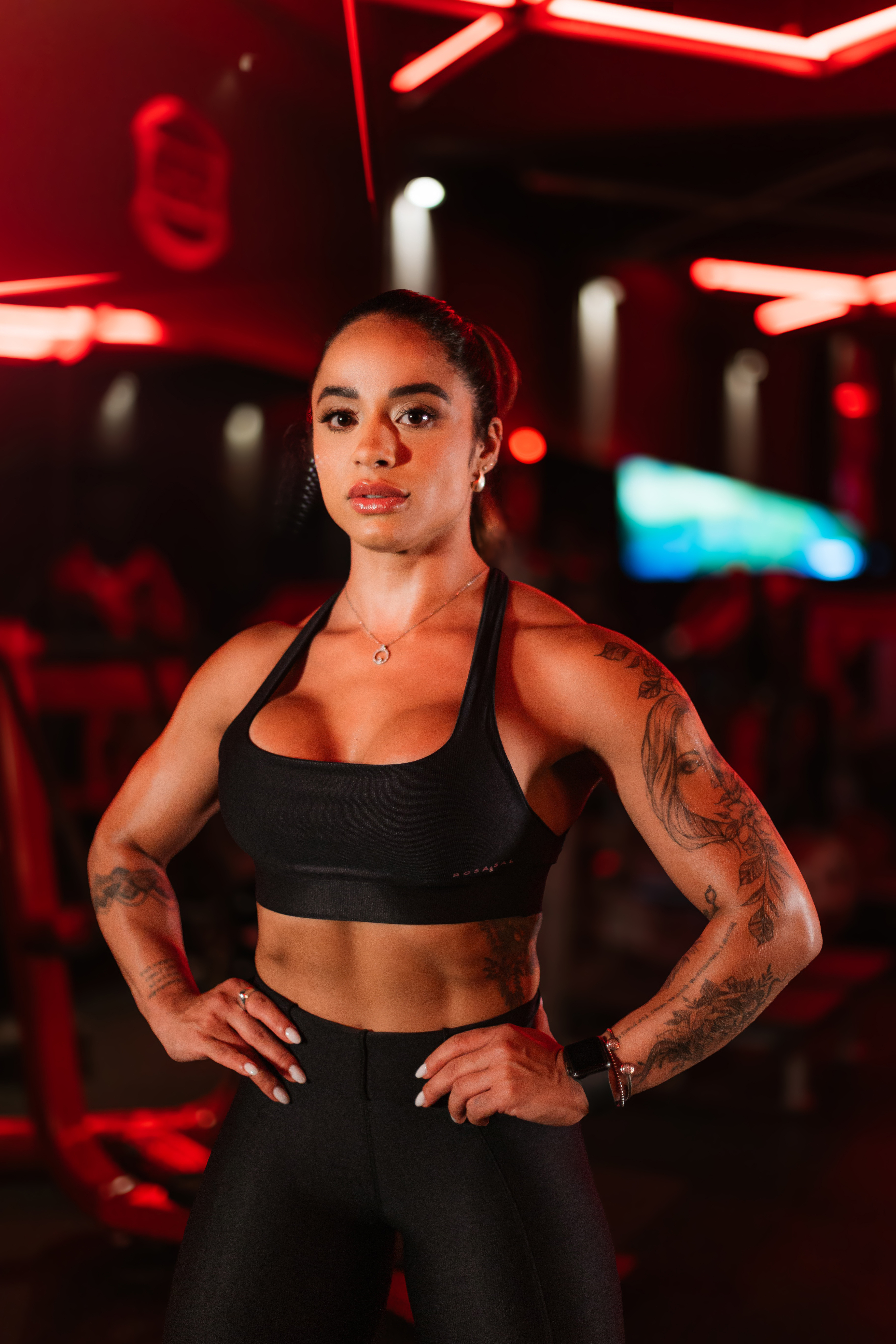 Fernanda Ferreira, personal trainer, de pé na academia com o neon vermelho ao fundo